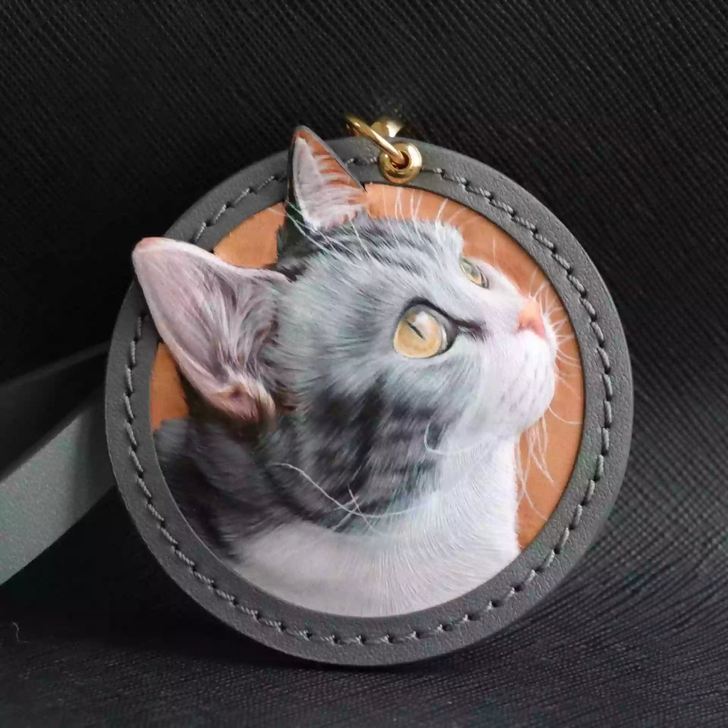 Custom leather cat portrait keychain in a round stitched frame on a dark background.
