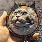 Hand holding a realistic 3D leather cat portrait keychain with metal clasp.

