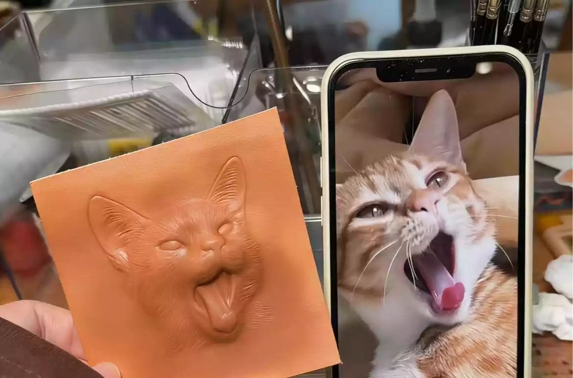 Close-up of a custom embossed leather cat portrait next to the matching reference photo on a phone