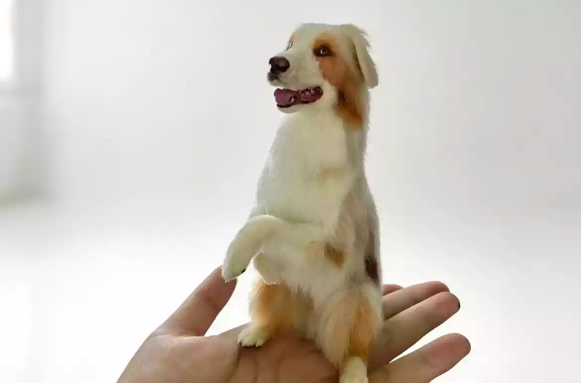 Hand holding a miniature needle-felted dog figurine against a bright background.